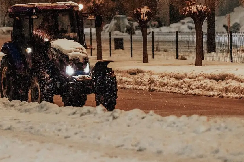 Traktor med plogblad framför en uppskottad snövall